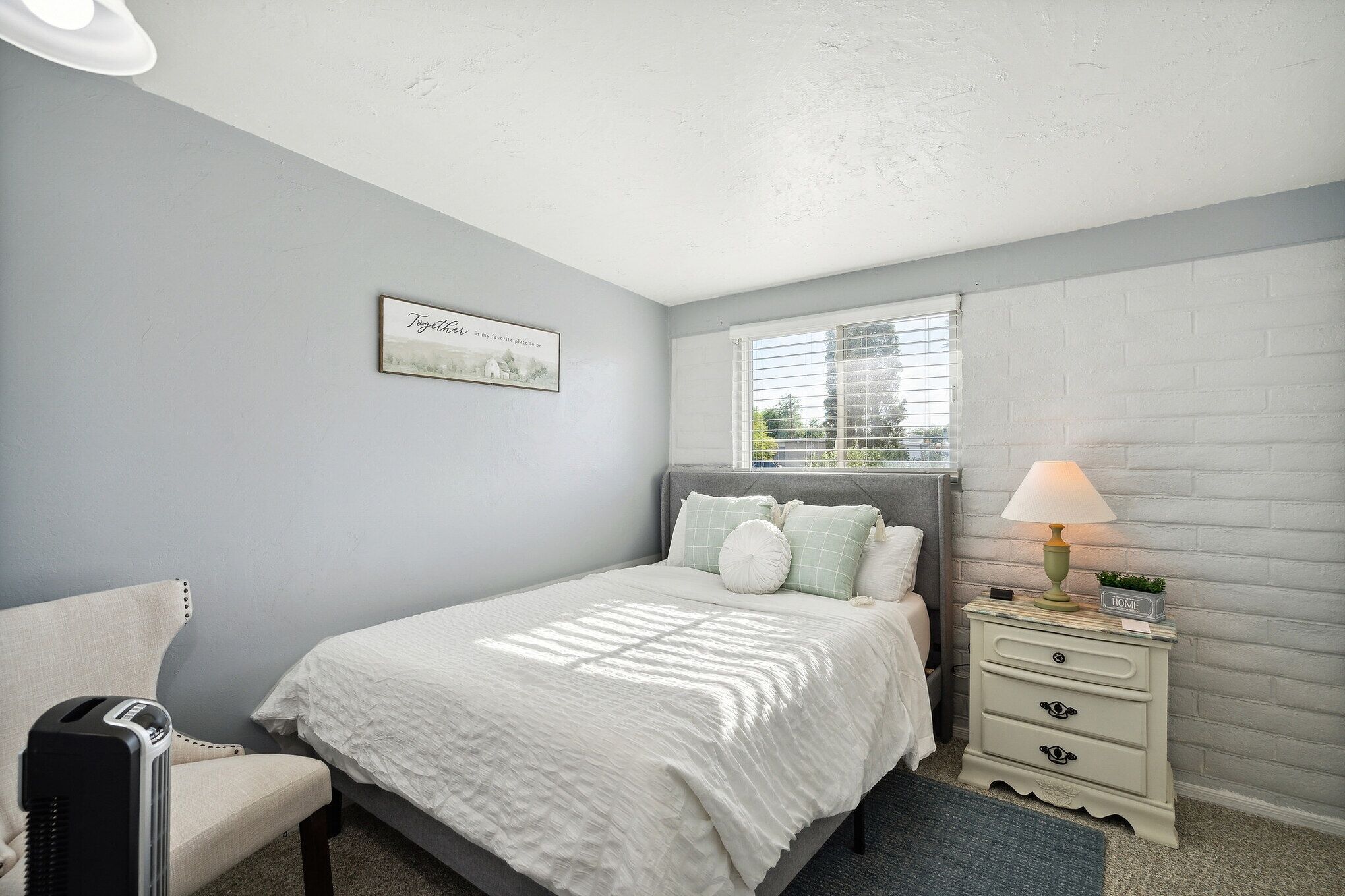 A bedroom with a bed, a nightstand, a lamp, and a chair.