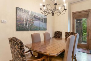 A dining area with a wooden table and six upholstered chairs, a chandelier, and a large painting of trees and flowers on the wall. - B107 Beaver Creek Landing 3 Bedroom Condo by RedAwning (Avon)
