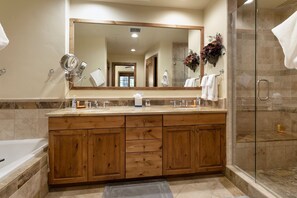 A modern bathroom with a large mirror, wooden vanity, a bathtub, and a glass-enclosed shower. - B107 Beaver Creek Landing 3 Bedroom Condo by RedAwning (Avon)