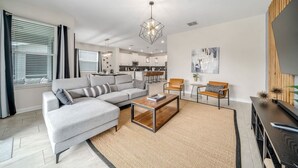 A modern living room with a grey sectional sofa, a wooden coffee table, and a dining area in the background. - 6BR getaway w/ pool, hot tub & game room (Four Corners)