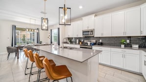 A modern kitchen with a large island, white cabinets, and a bar area with orange chairs. - 6BR getaway w/ pool, hot tub & game room (Four Corners)