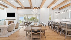 A spacious dining area with a long wooden table and chairs, a fireplace, and a large window offering a view of the outdoors.