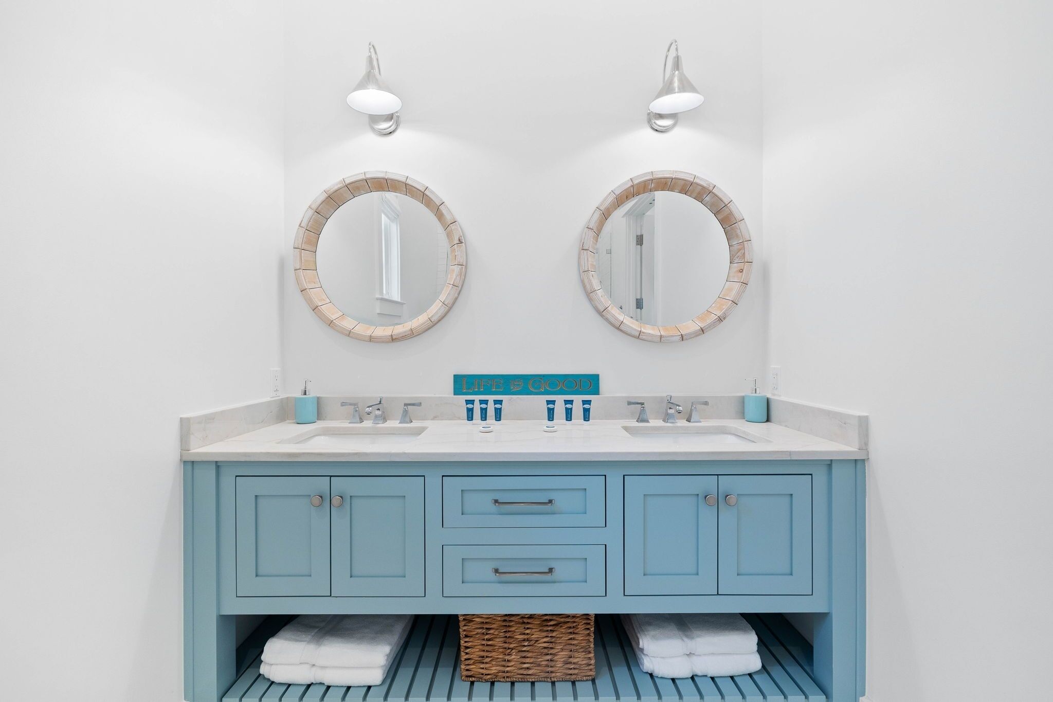A bathroom with two mirrors, a blue vanity, and a towel rack.