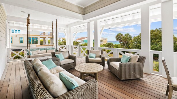 A covered outdoor seating area with wicker furniture and a view of the ocean.
