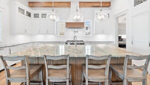 A spacious kitchen with a large island, white cabinetry, and a wooden ceiling.