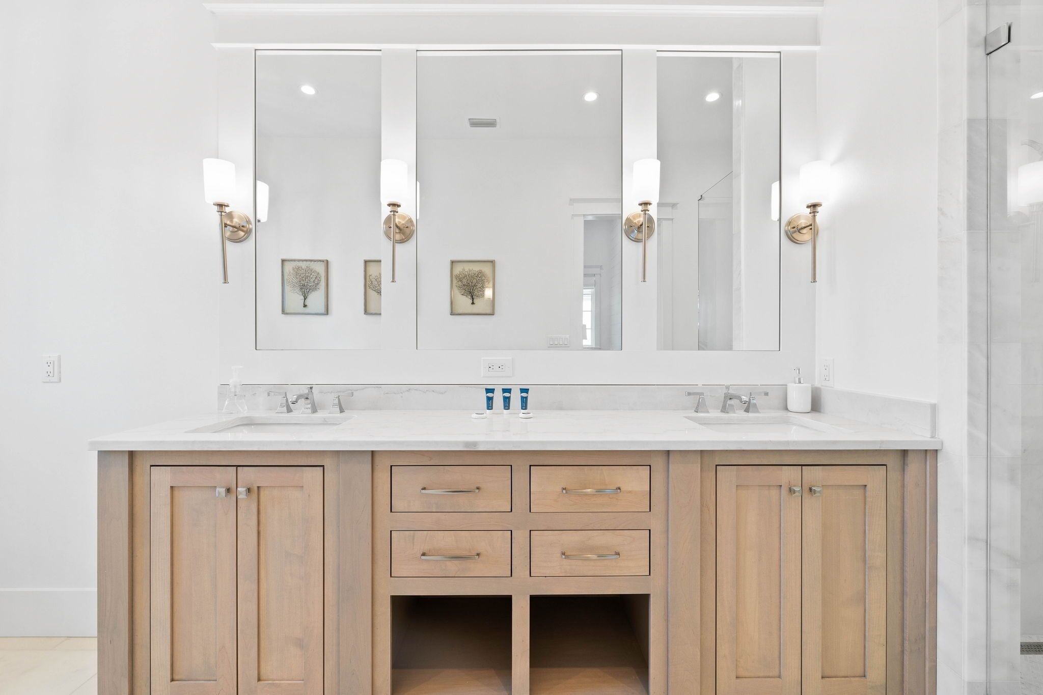 A modern bathroom with a large mirror, two sinks, wooden cabinets, and wall-mounted lights.