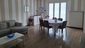 Una sala de estar con un sofá gris, una mesa de centro blanca y una zona de comedor con una mesa redonda y sillas.