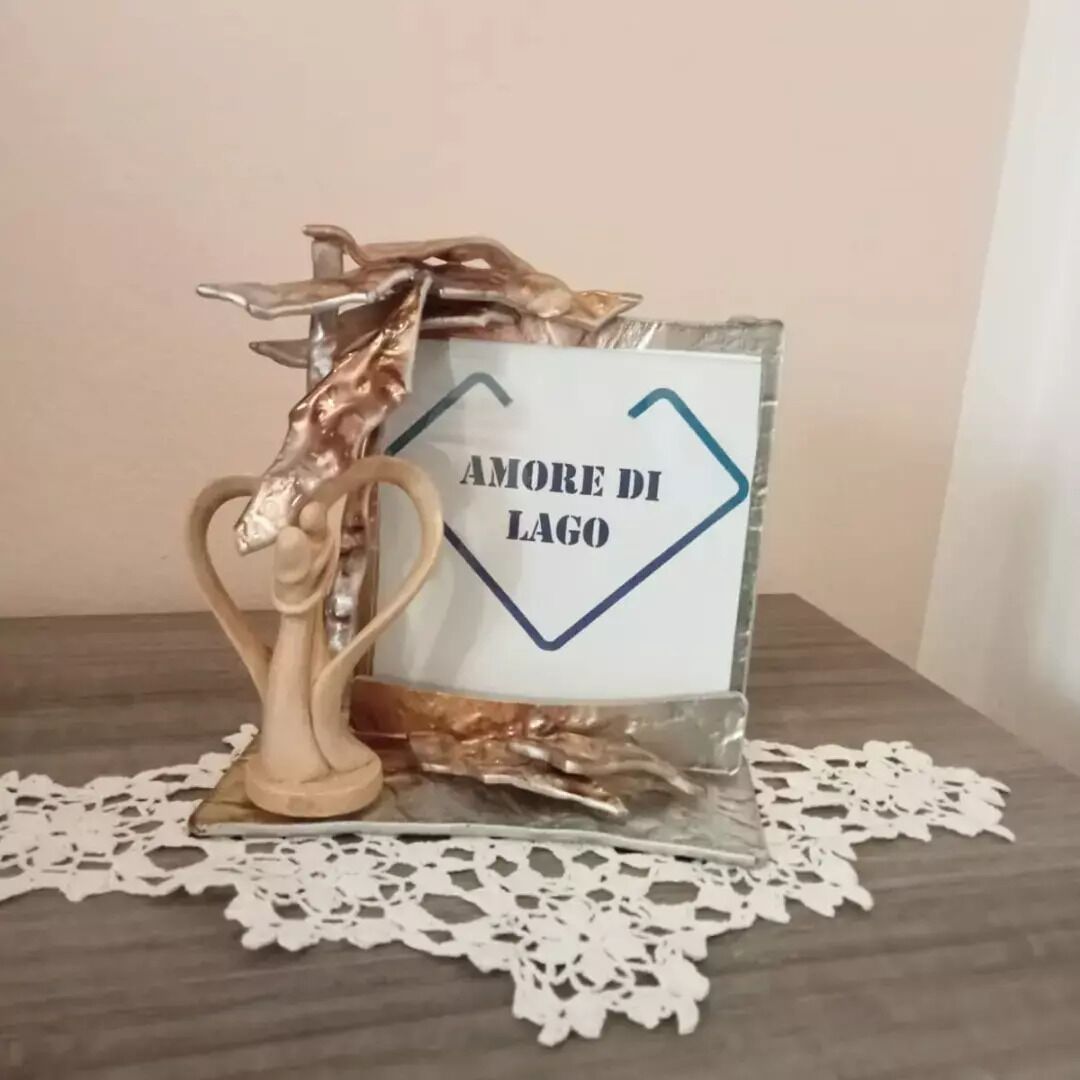 Un panneau décoratif portant l’inscription « AMORE DI LAGO », entouré d’éléments métalliques et d’une dentelle blanche en forme de napperon.