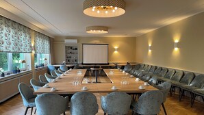 A conference room with a long table, grey upholstered chairs, a projector screen, and a patterned wall. - Hotel Restaurant Steinhägerquelle (Steinhagen)