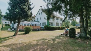 A large building with a white facade and green trim, surrounded by trees and a grassy area. - Hotel Restaurant Steinhägerquelle (Steinhagen)