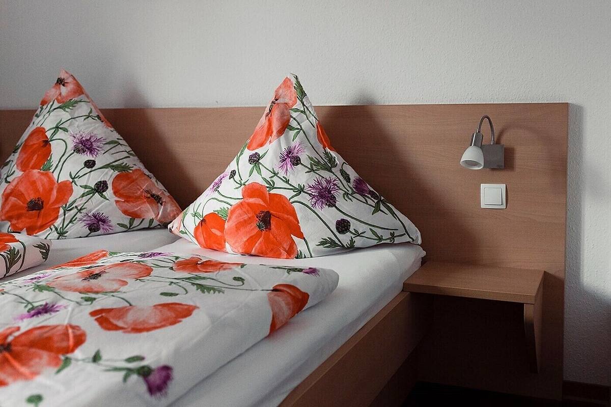 Ein ordentlich gemachtes Bett mit blumigem Kissenmuster und einem Nachttisch mit Lampe.