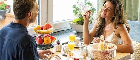 Un comedor con una mesa dispuesta para dos personas, un frutero, una taza de café y una cesta de pan.