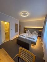 Un dormitorio con cama, mesitas de noche, una silla, una pequeña mesa y una lámpara en el techo.