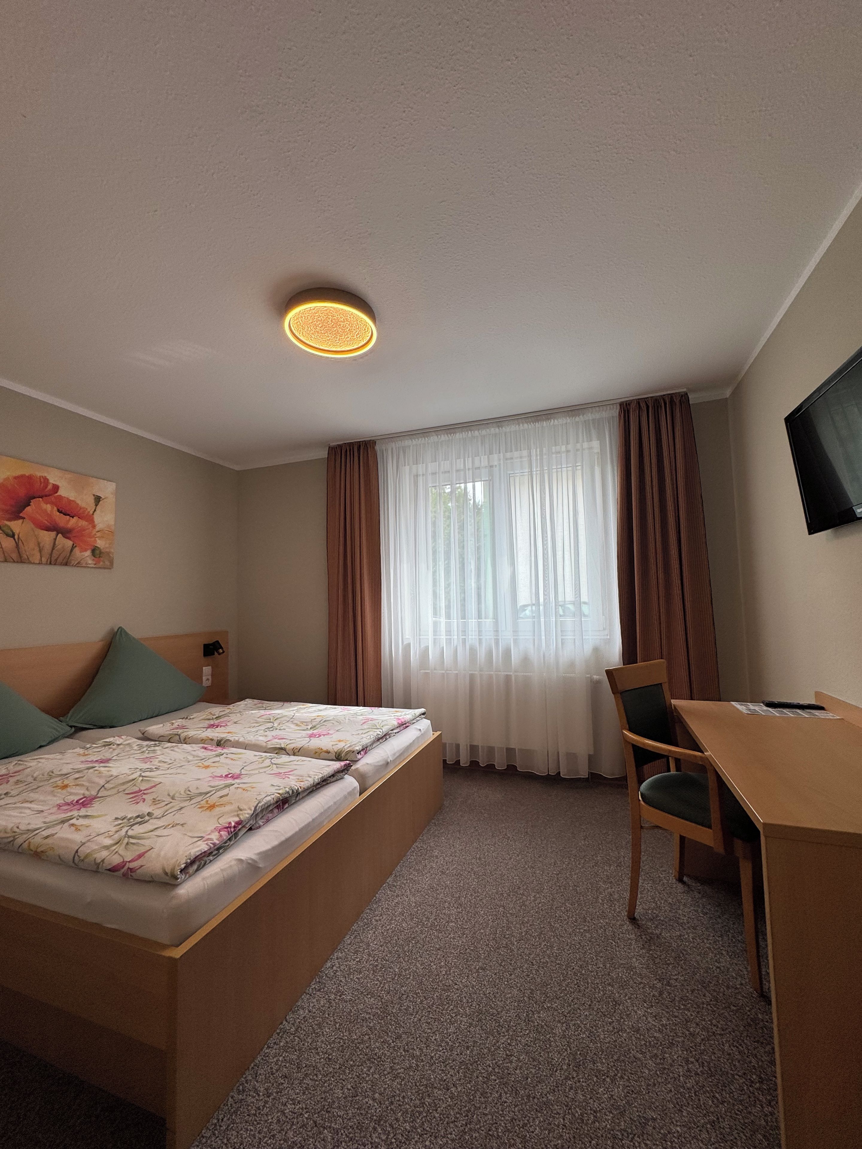 A hotel room with a bed, a desk, a chair, a television, and a painting on the wall.