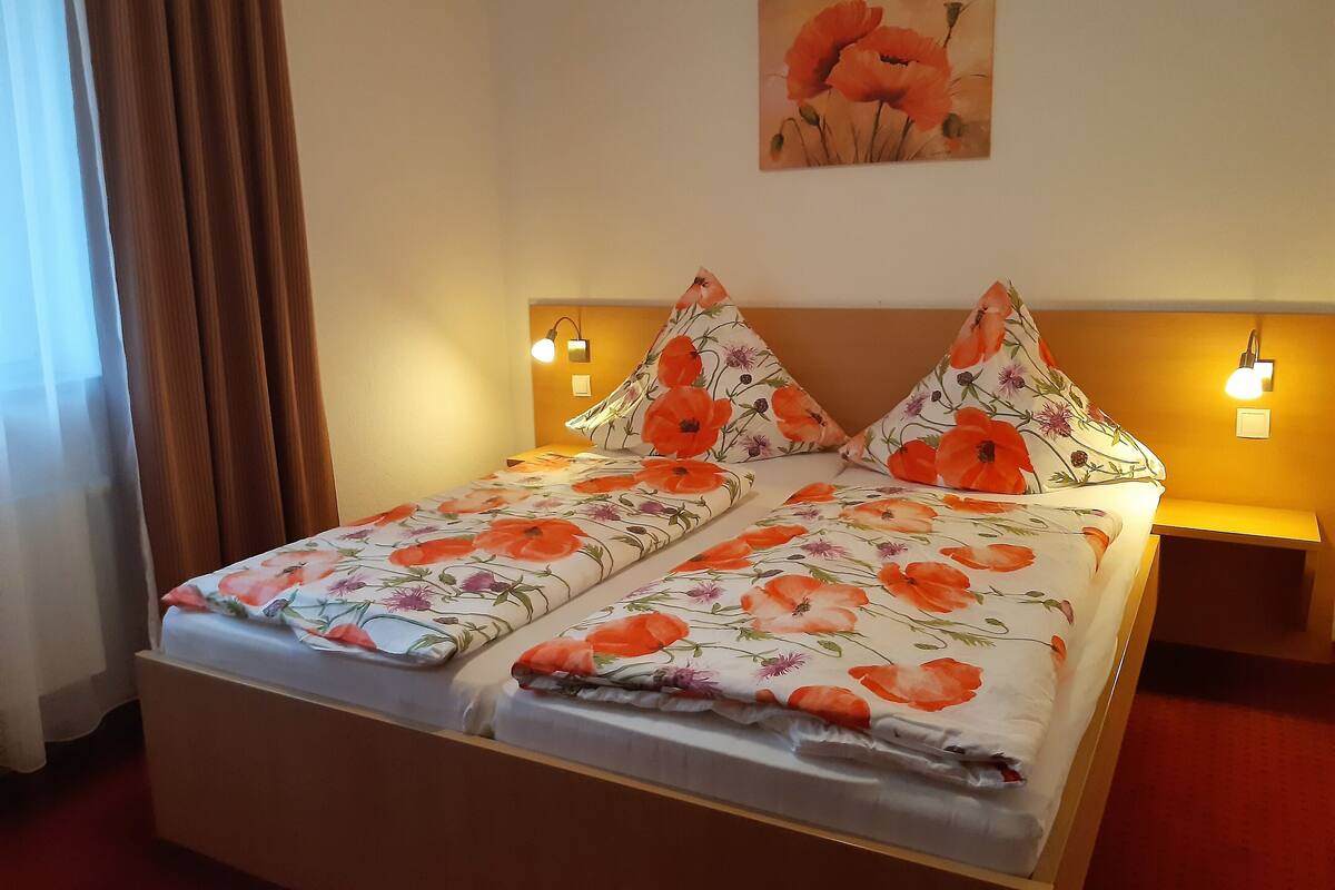 Ein Doppelbett mit blumigem Bettzeug, zwei Nachttischlampen und ein Bild an der Wand.