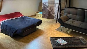 Ein Schlafzimmer im Loft-Stil mit schrägem Dach, Holzbalken, einem Bett, einer Couch und einem kleinen Tisch.