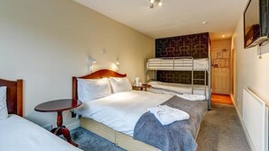 Une chambre d’hôtel avec un lit simple, une petite table, un lit superposé et un téléviseur.