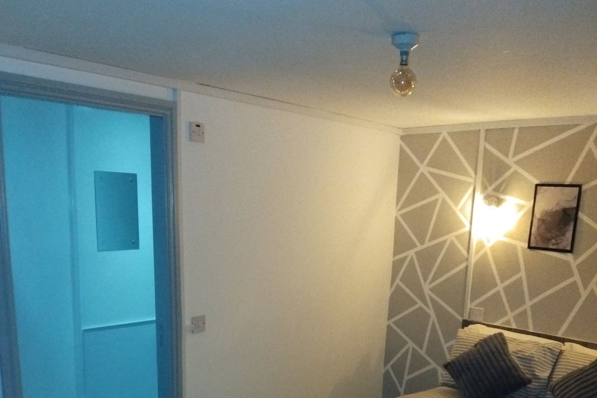 A bedroom with a bed, pillows, and a wall-mounted light fixture.