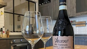A bottle of Amarone wine on a wooden table with two empty wine glasses.