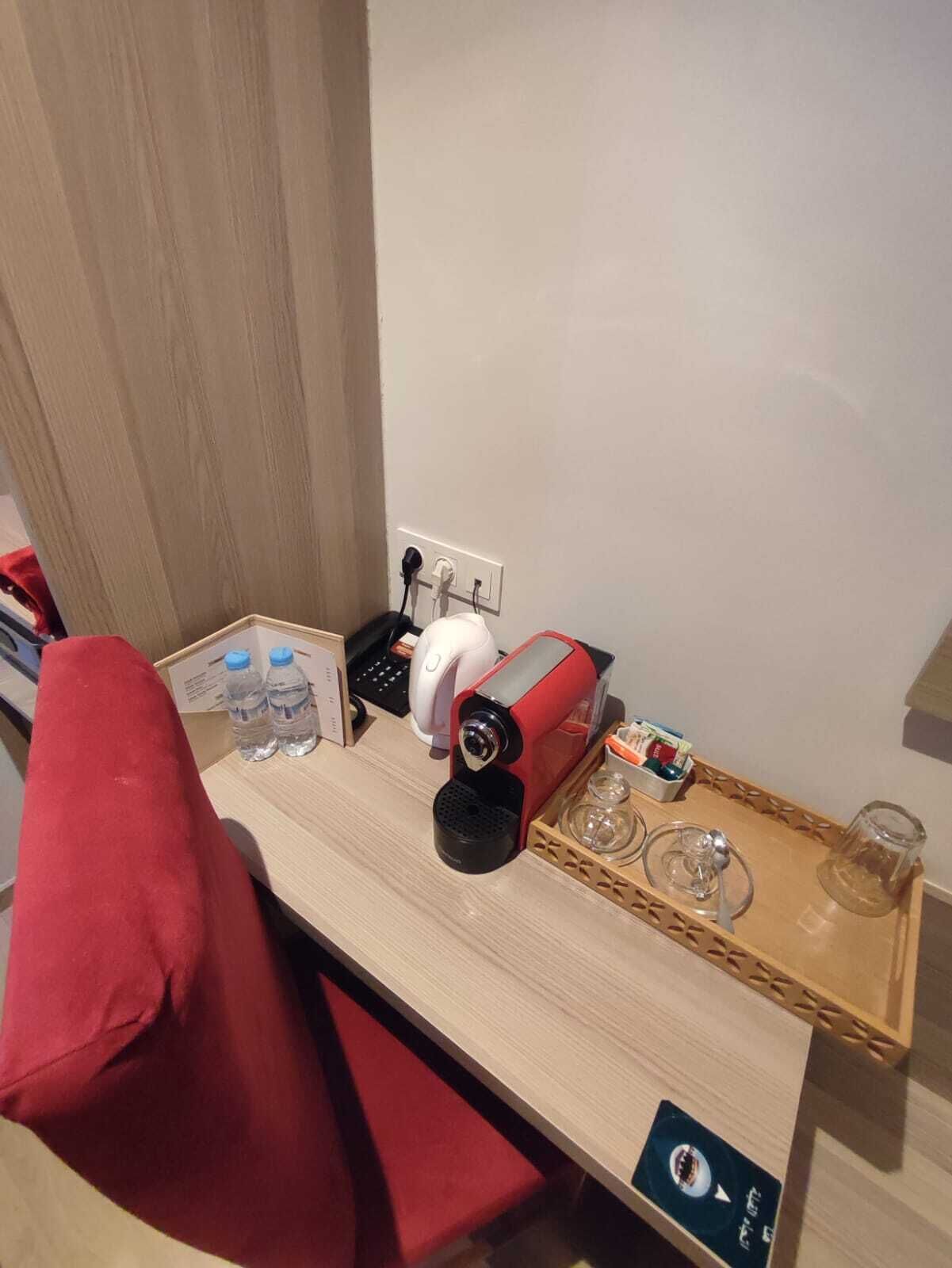 A small kitchenette with a coffee maker, water bottles, and a tray with glasses and a glass.