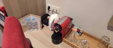 A small kitchenette with a coffee maker, water bottles, and a tray with glasses and a glass.