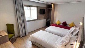 A hotel room with two beds, a desk, a chair, a TV, and a window with curtains. - Hotel Al Fajr (Oujda)