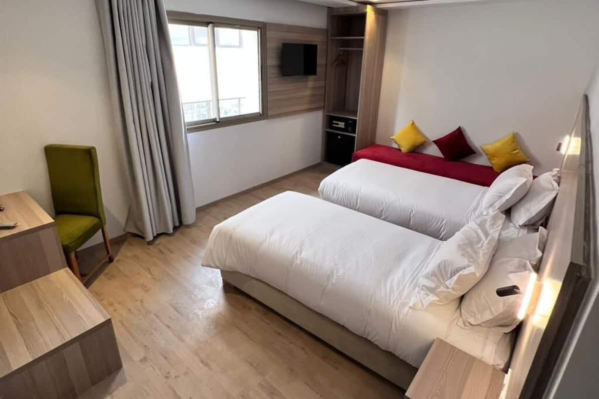 A hotel room with two beds, a desk, a chair, a TV, and a window with curtains.