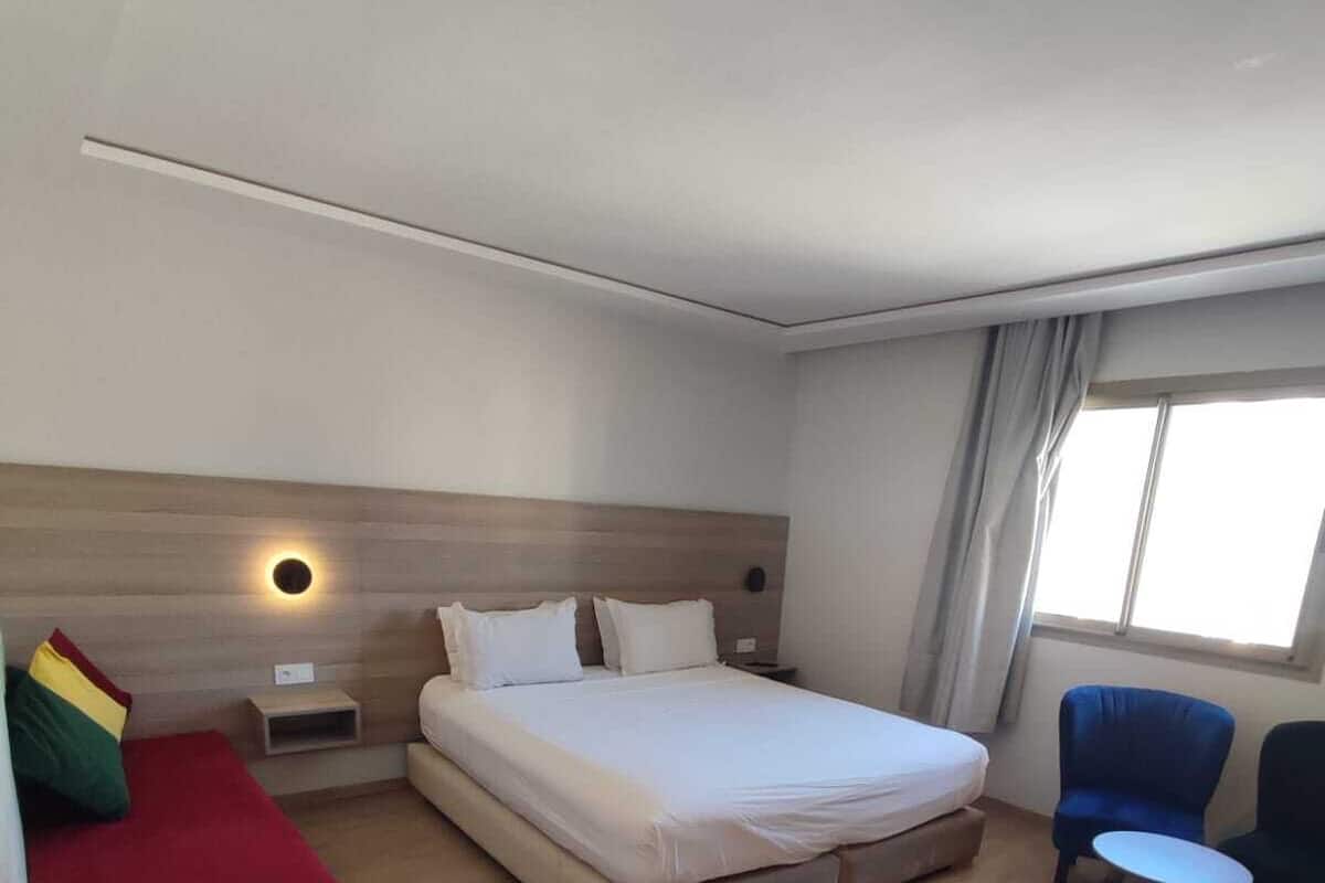 A hotel room with a bed, a small table, a chair, and a window.