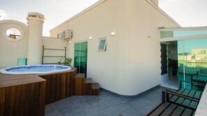 Una terraza en la azotea con jacuzzi, asientos de madera y un ventanal que da a un balcón.