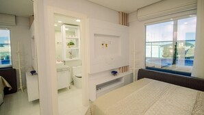 Una habitación de hotel moderna con una cama grande, televisión integrada, baño pequeño con inodoro y lavamanos, y ventana con vista a la ciudad.