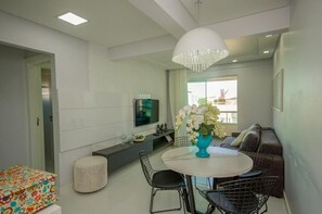 Uma sala de estar moderna com uma mesa de jantar redonda, um sofá, uma televisão e um candelabro.