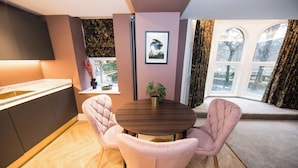 Une cuisine moderne avec une table de salle à manger ronde, des chaises recouvertes d’un tissu rose et une fenêtre avec des rideaux.