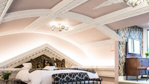 Ein Schlafzimmer mit schrägen Wänden, einem Bett mit weiß-schwarz gemustertem Kopfteil, einer kleinen Couch und einer dekorativen Deckenleuchte.
