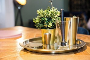 Een dienblad met een cocktailshaker, een glas en een metalen beker op een houten tafel.