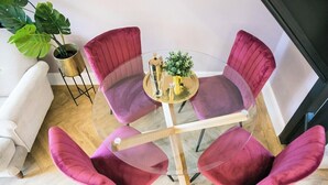 A round glass table with four purple chairs, a small potted plant, and a gold-colored object on the table.
