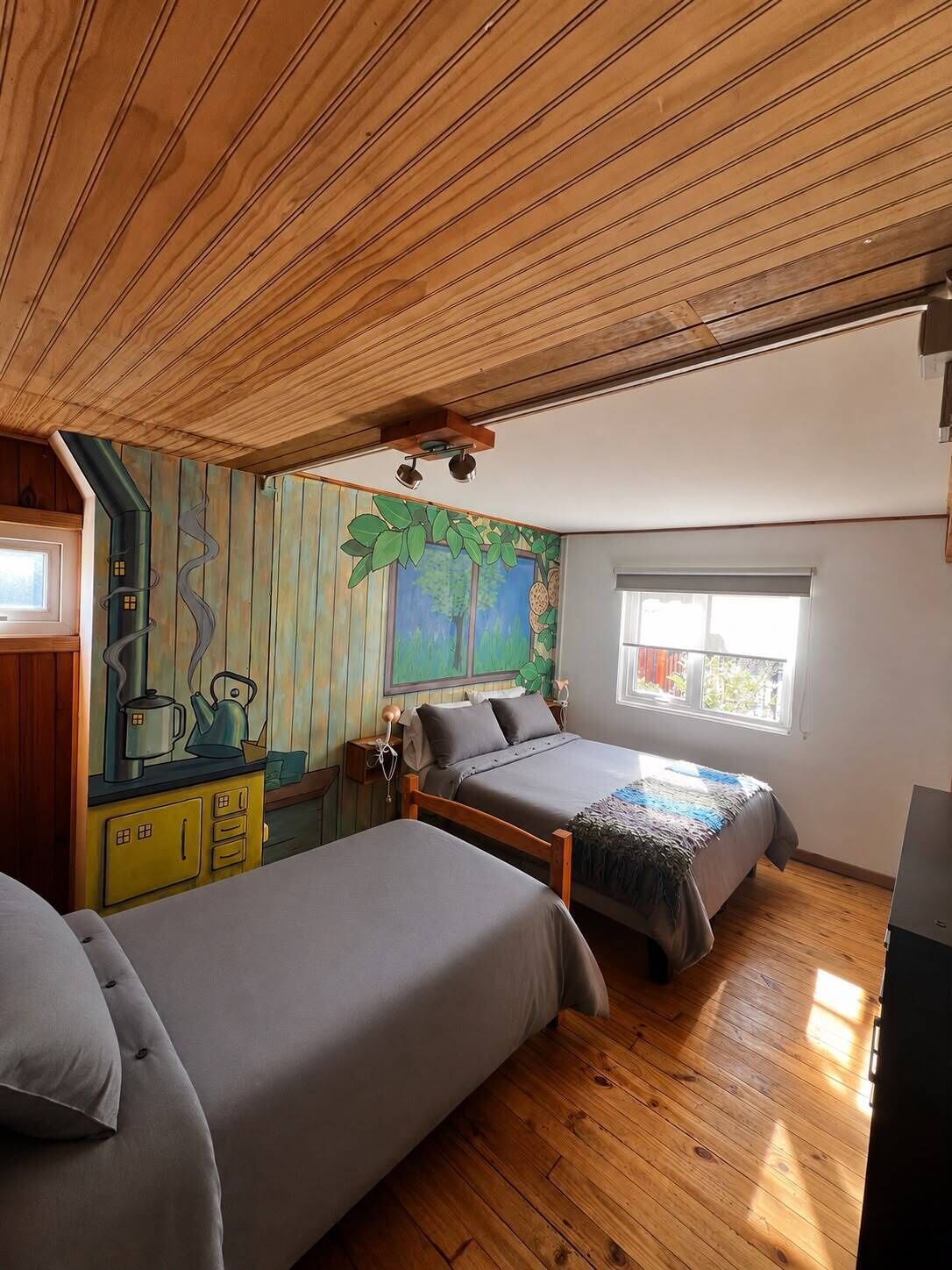 Ein Schlafzimmer mit zwei Betten, Holzböden, einem Fenster und einem Wandgemälde.