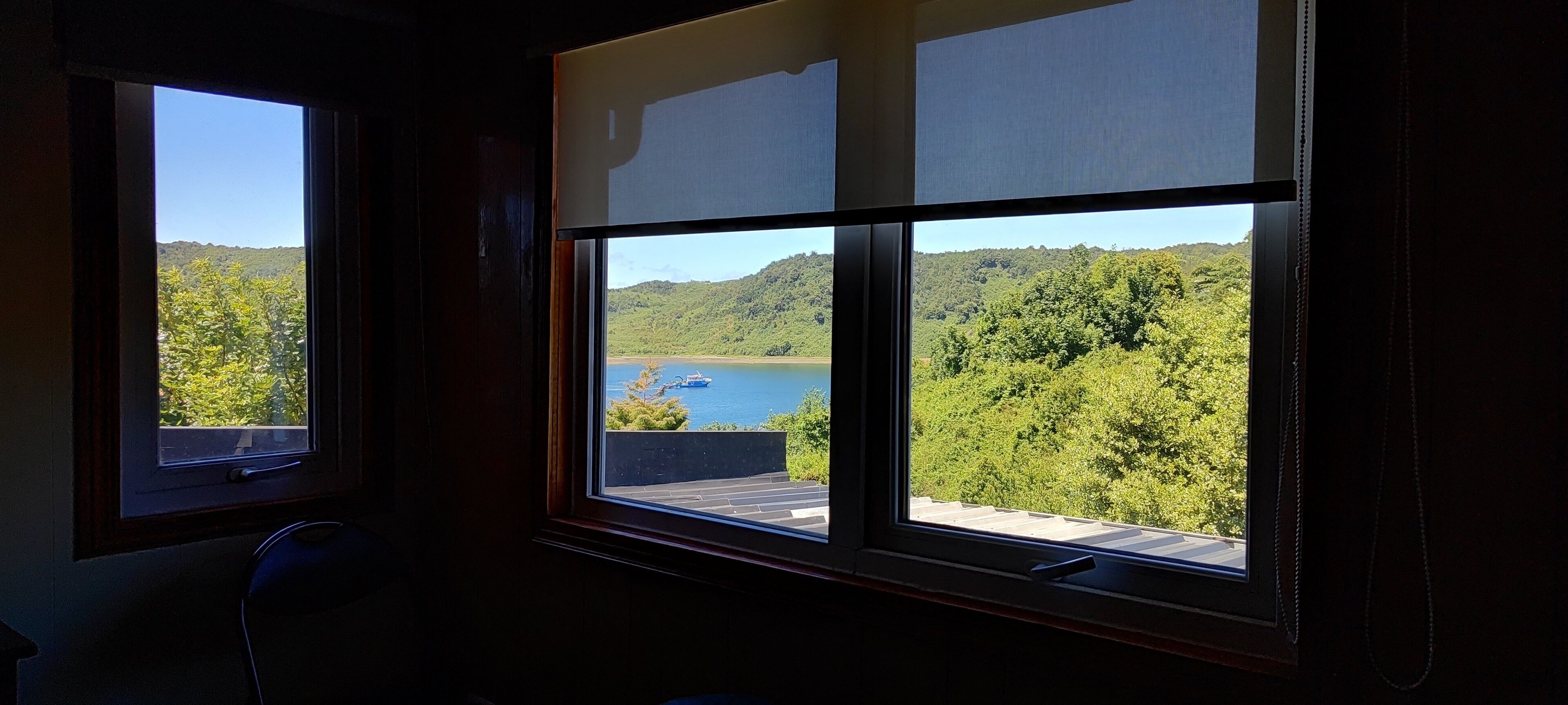Quarto com duas janelas com vista para um lago e colinas arborizadas.