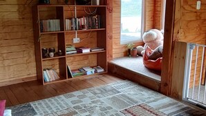 Una habitación acogedora con un ventanal grande, una estantería, un rincón de estar con cojines y una alfombra estampada.
