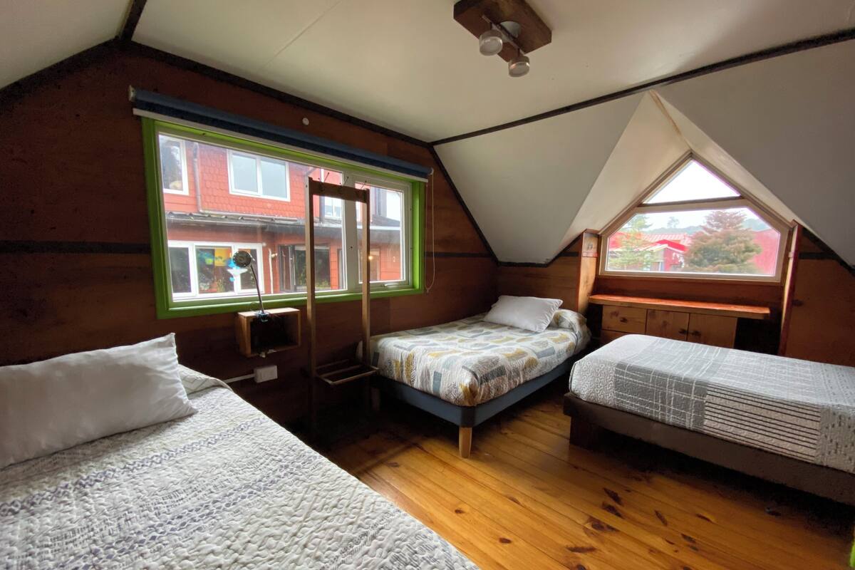 Ein kleines, dreieckiges Schlafzimmer im Dachgeschoss mit zwei Betten, Holzboden und einem Dachfenster.