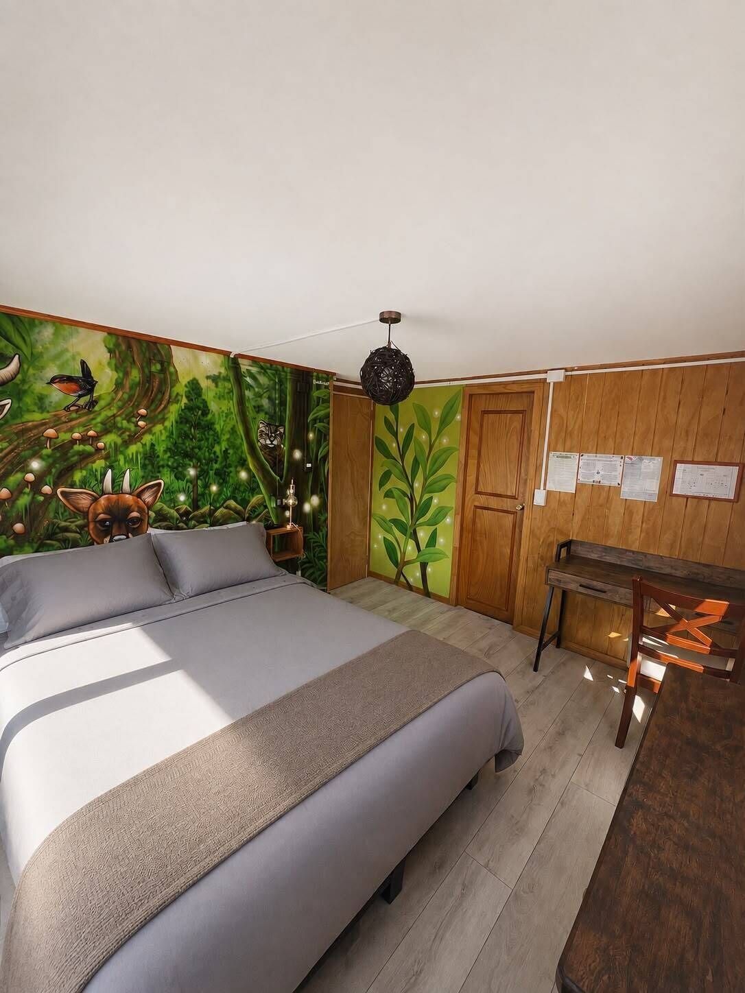 A bedroom with a bed, a desk, and a wall mural.