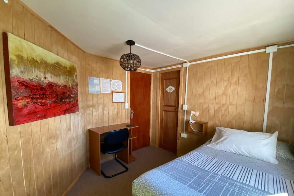 Ein Zimmer mit Bett, Schreibtisch, Stuhl und einem Bild an der Wand.