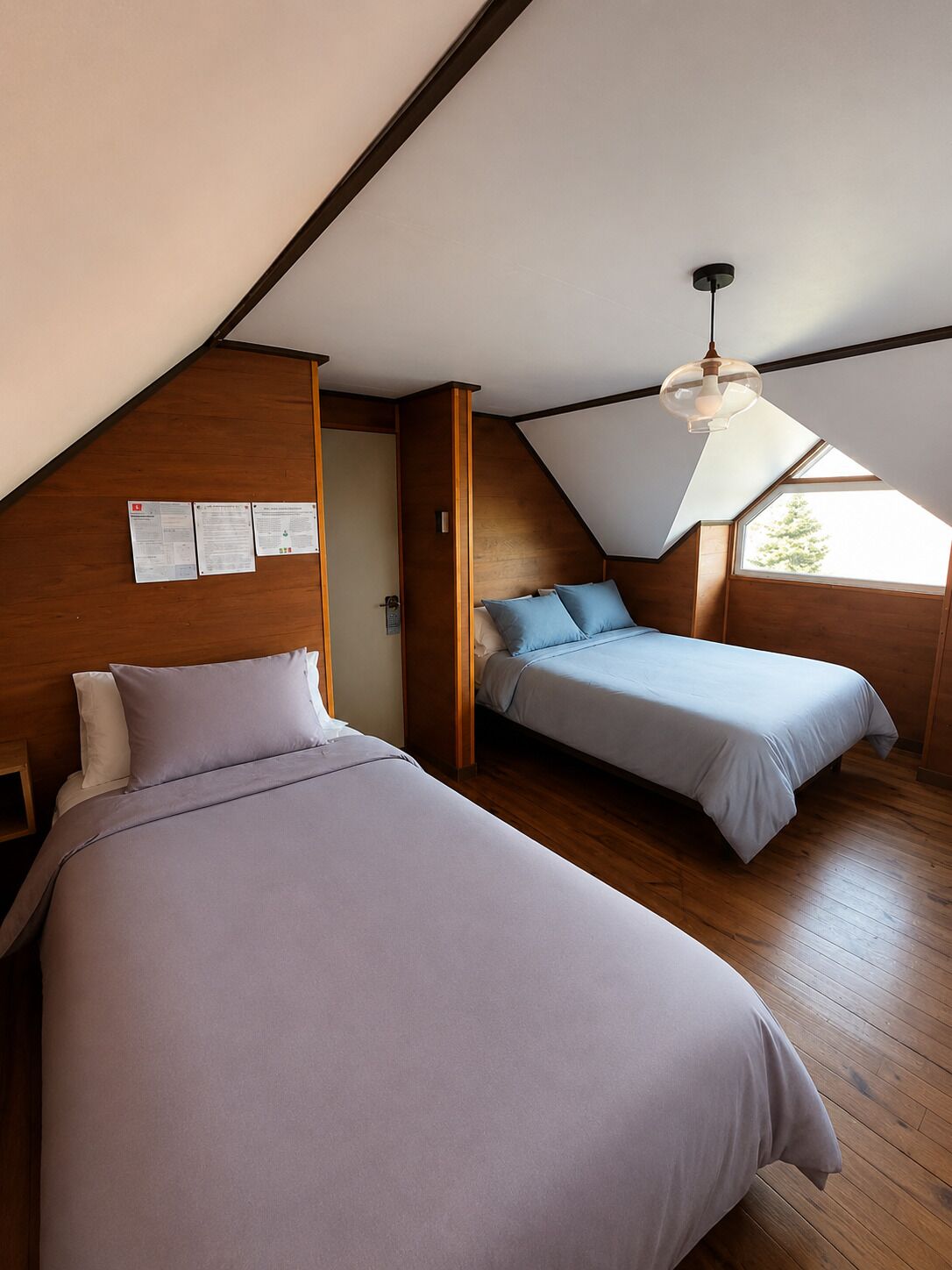 A room with two beds, wooden walls, a sloped ceiling, and a skylight.