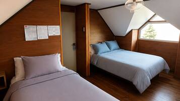 A room with two beds, wooden walls, a sloped ceiling, and a skylight.