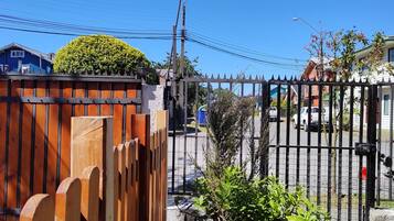 A gated area with a wooden fence and a metal gate, a blue building, and a white building with a sign.
