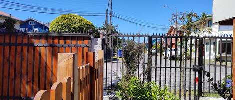 Un área cercada con valla de madera y portón metálico, un edificio azul y un edificio blanco con un letrero.