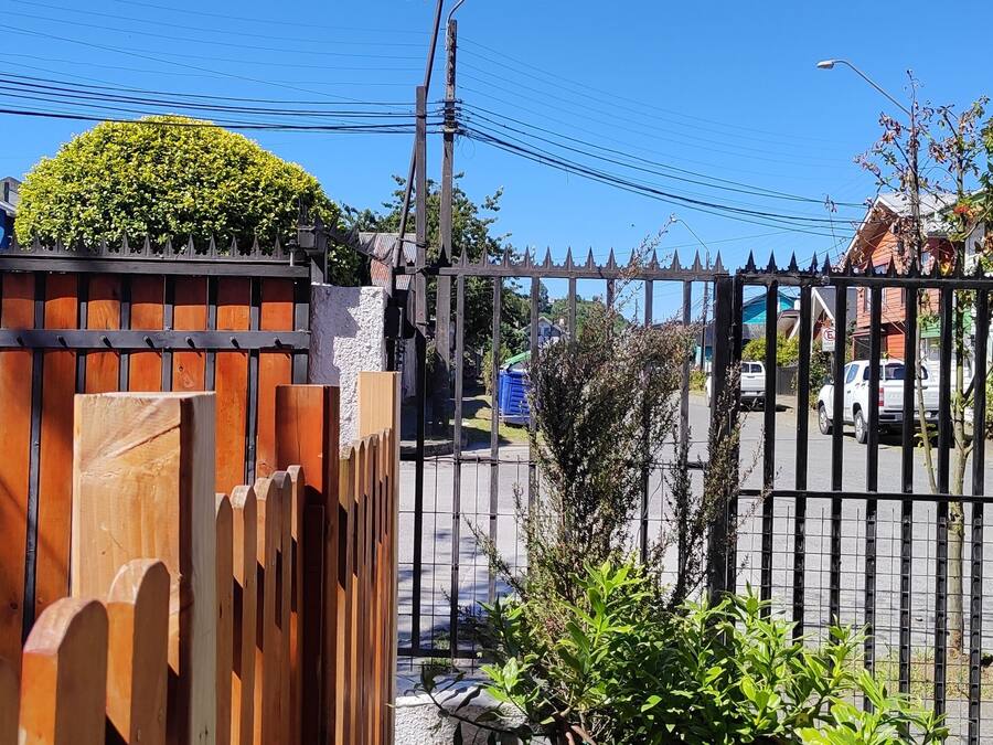 A gated area with a wooden fence and a metal gate, a blue building, and a white building with a sign.