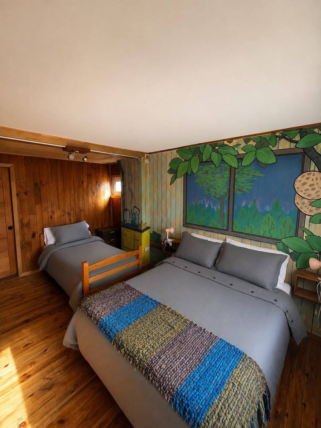 A bedroom with a large bed, two bedside tables, a wooden wardrobe, and a mural of a forest scene.