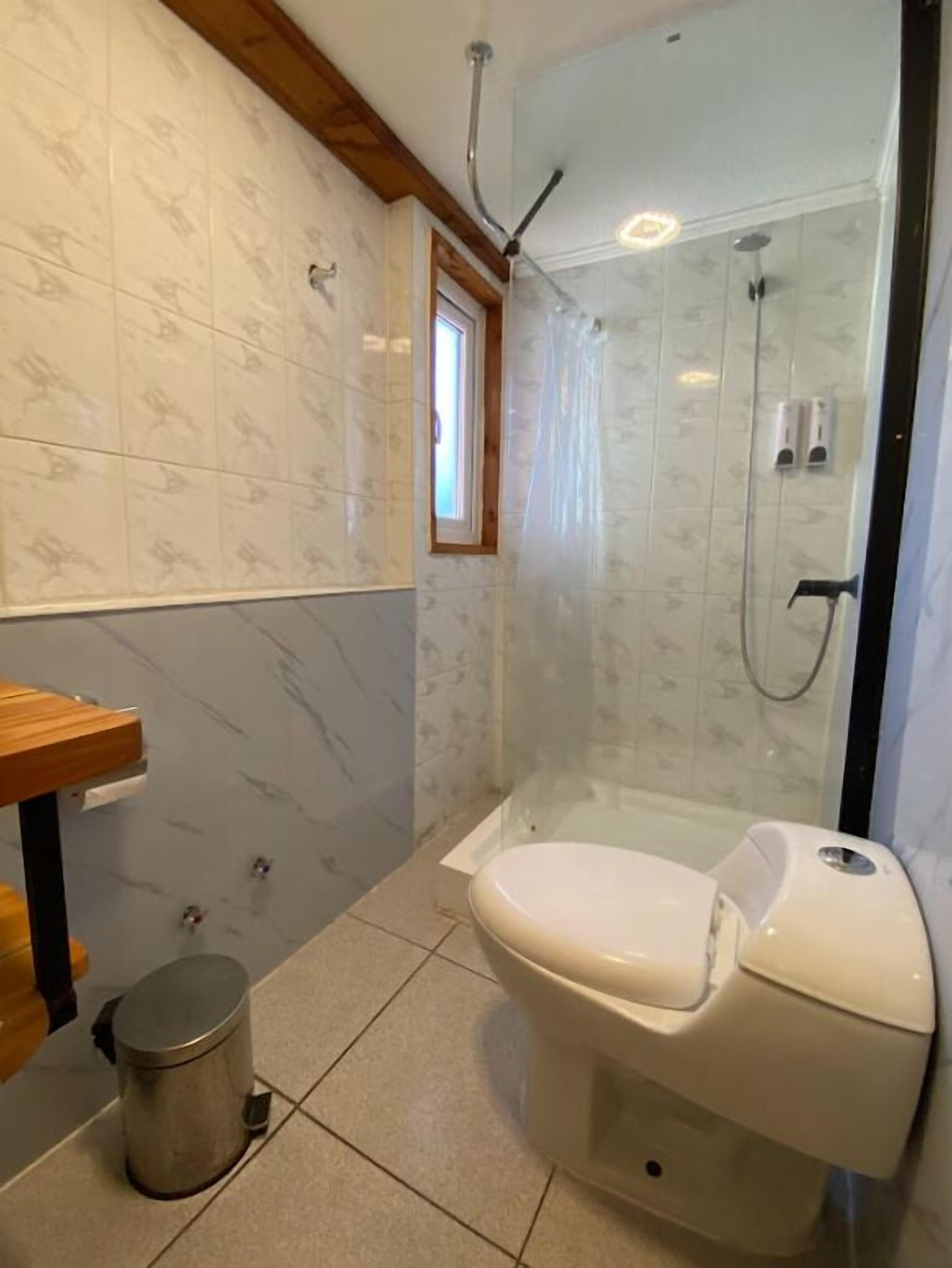 Et badeværelse med toilet, bruser og et lille vindue.