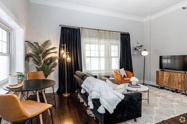 A modern living room with a black sofa, a round coffee table, a TV stand, and a potted plant.
