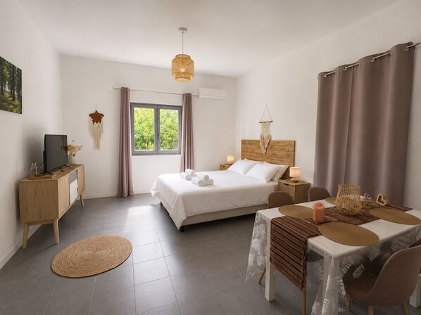 Ein Schlafzimmer mit Bett, Nachttischen, Schreibtisch, Stuhl, Esstisch und einem Fenster mit Vorhängen.